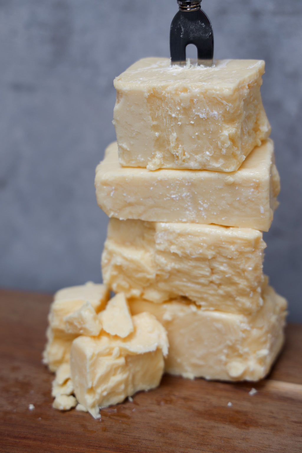 Stack of Aged Cheddar Offcuts from Eltham Cheese Bar on a wooden surface with a gray concrete background