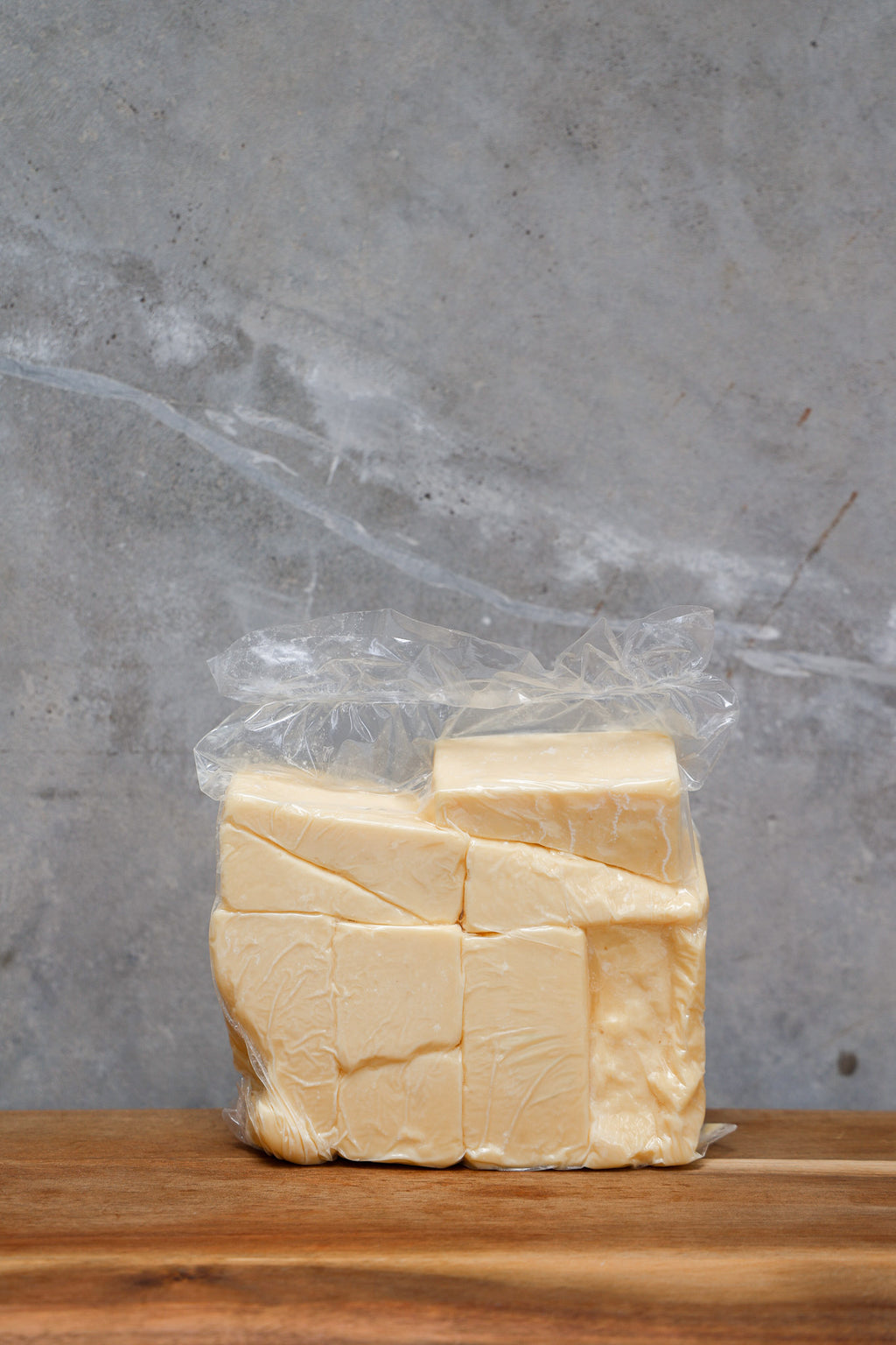 Block of Aged Cheddar Offcuts from Eltham Cheese Bar in a clear plastic bag on a wooden surface with a gray background