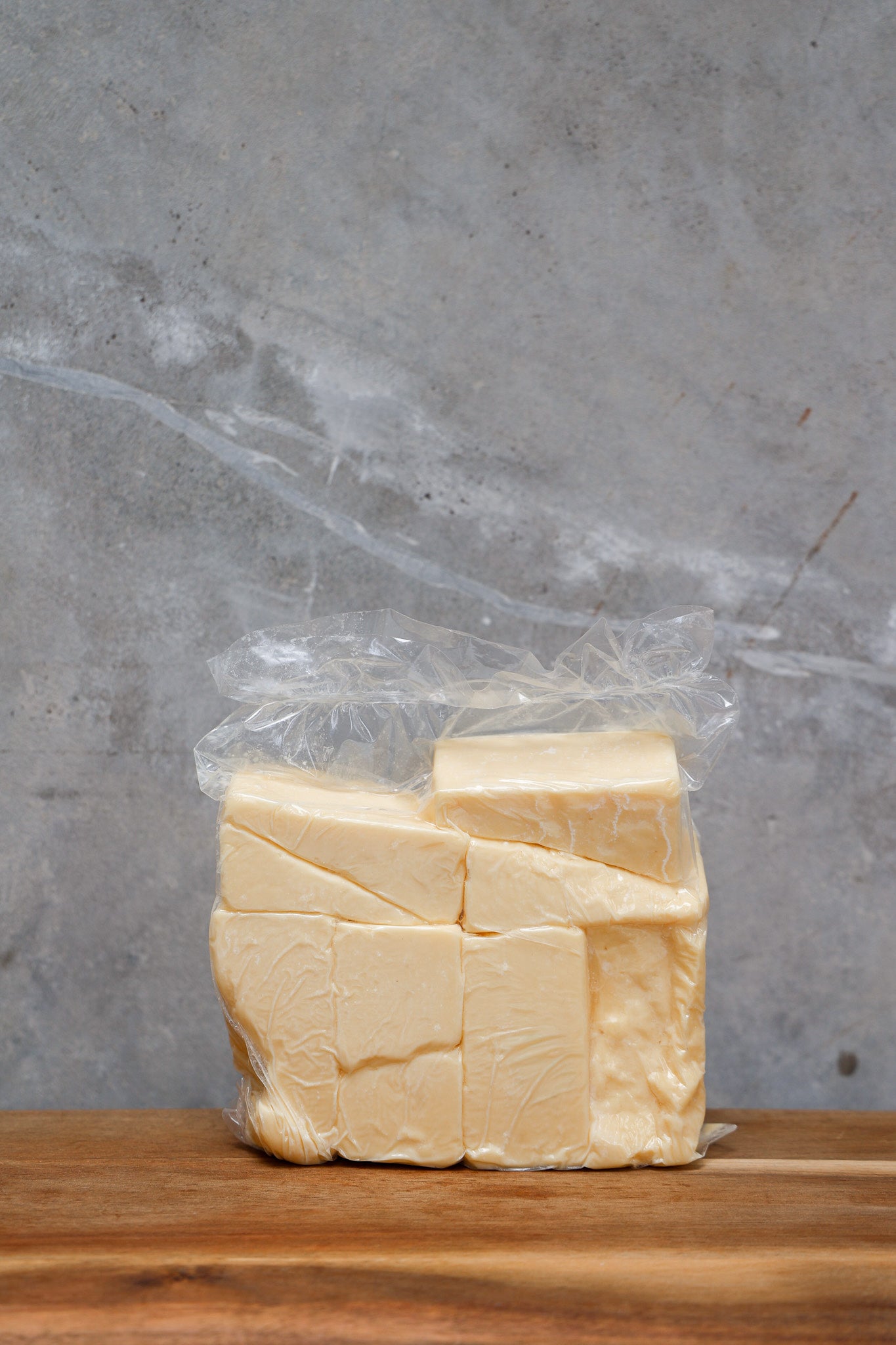 Block of Aged Cheddar Offcuts from Eltham Cheese Bar in a clear plastic bag on a wooden surface with a gray background