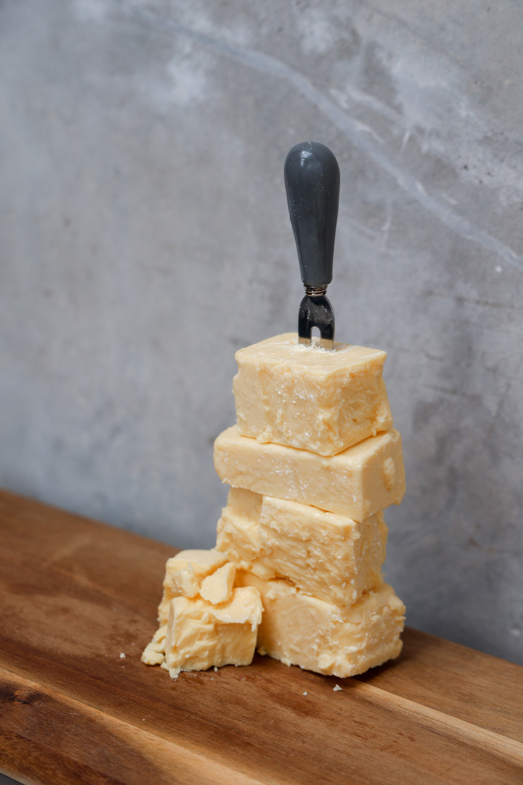 Stack of Aged Cheddar Offcuts from Eltham Cheese Bar on a wooden surface with a gray concrete background