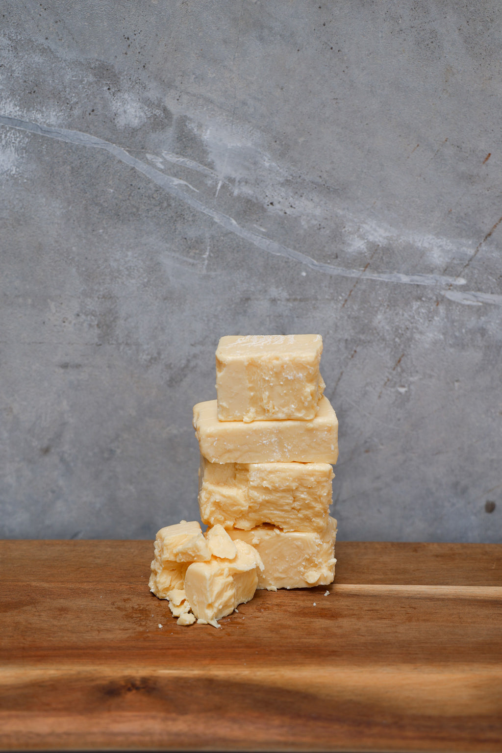 Stack of Aged Cheddar Offcuts from Eltham Cheese Bar on a wooden surface with a gray concrete background