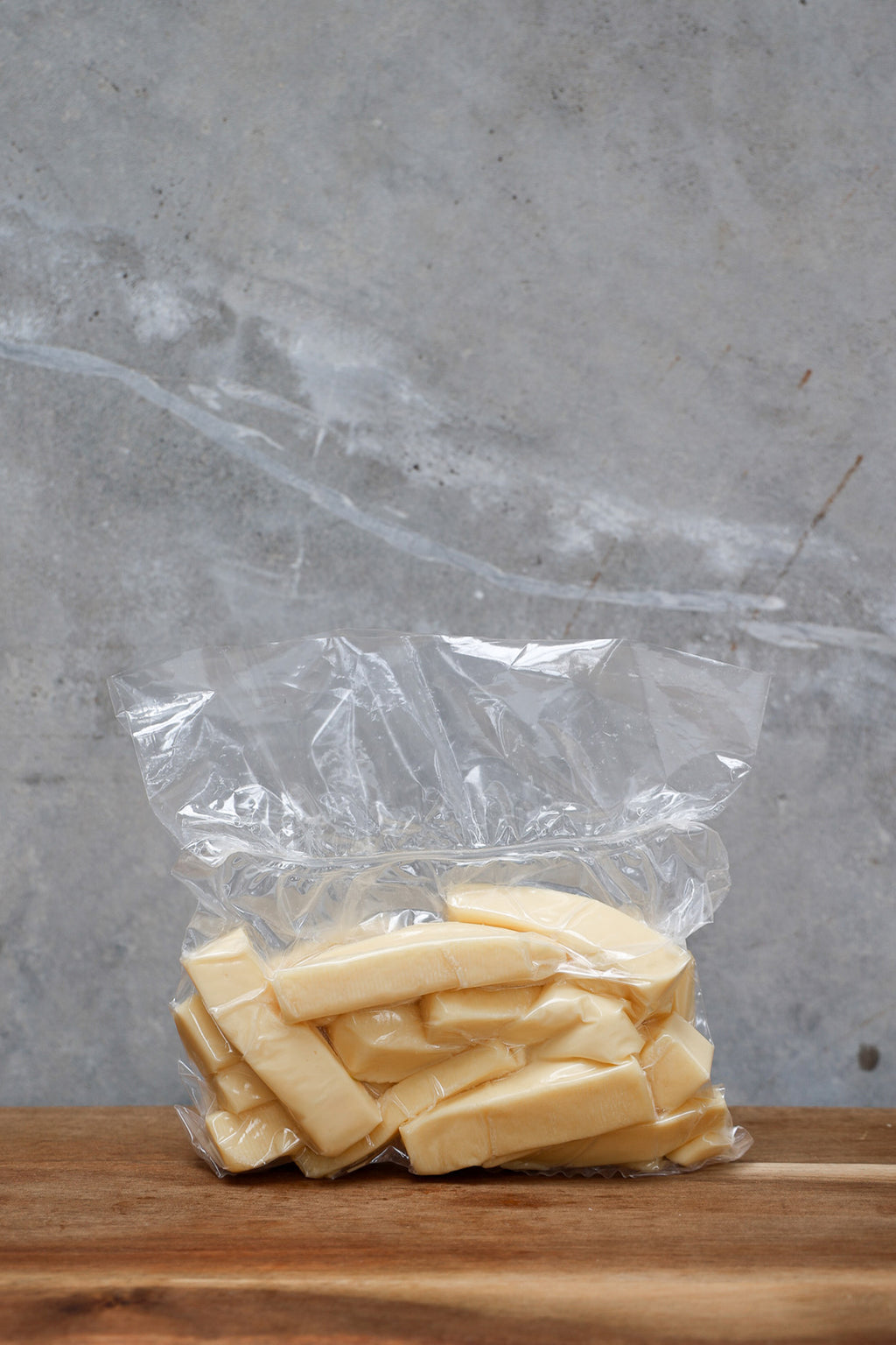 Block of Havarti Offcuts from Eltham Cheese Bar in a clear plastic bag on a wooden surface with a gray background