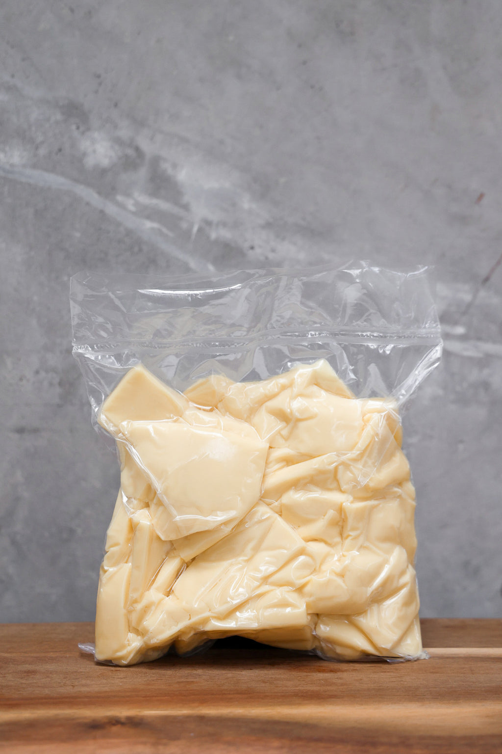 Block of Mozzarella Offcuts from Eltham Cheese Bar in a clear plastic bag on a wooden surface with a gray background
