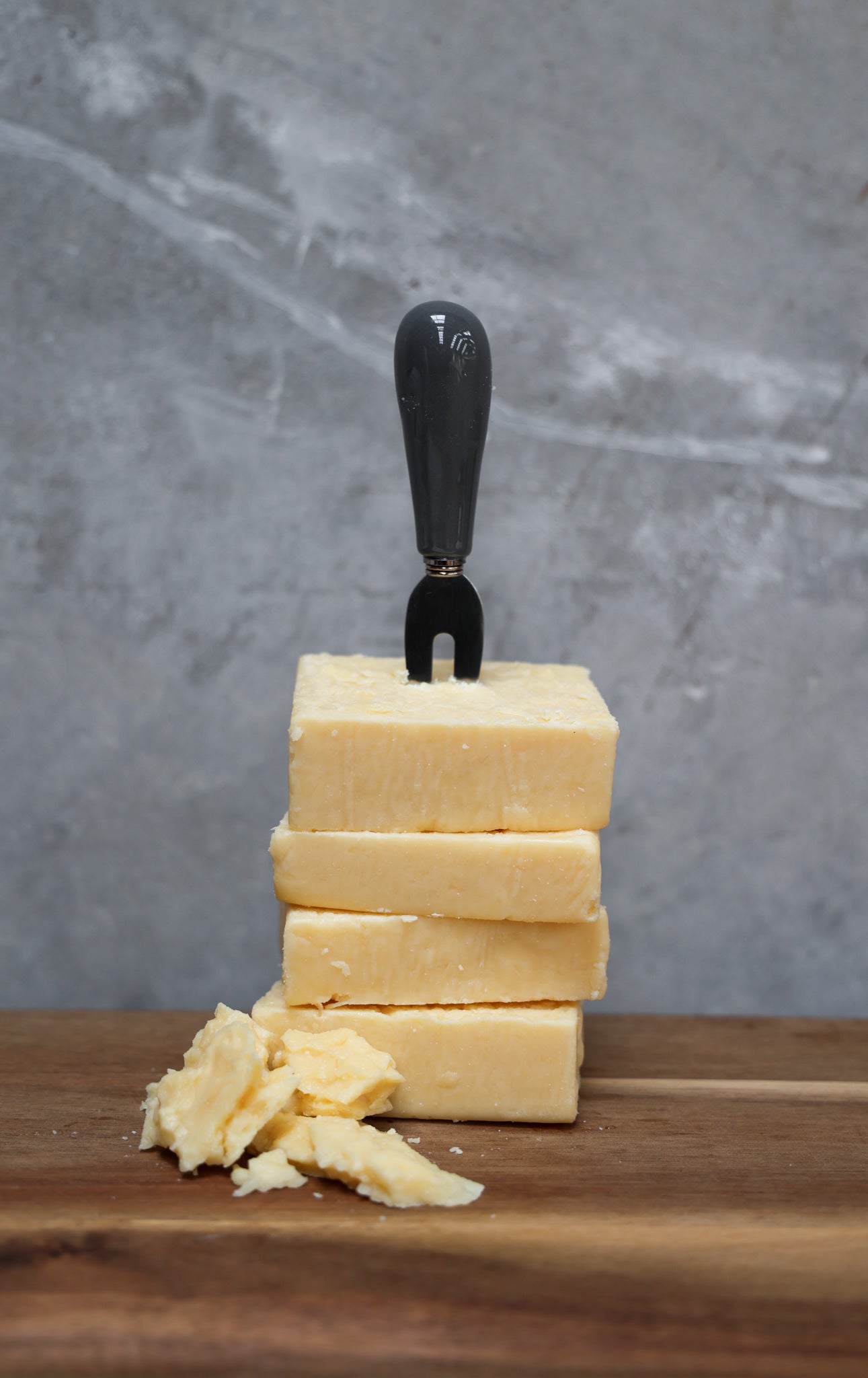 Stack of parmesan cheese blocks from Eltham Cheese Bar with a cheese knife on a wooden surface and gray background
