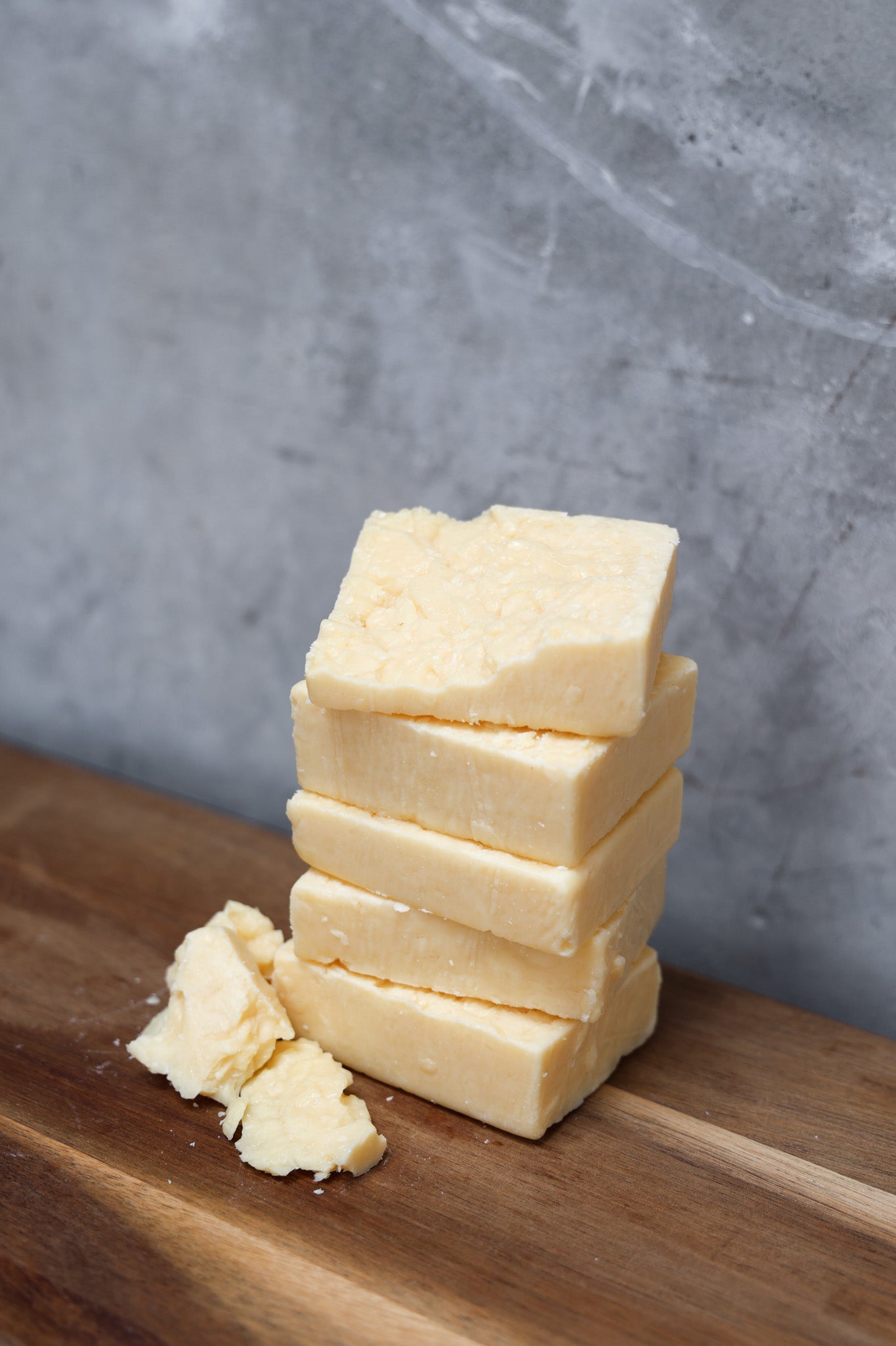 Stack of parmesan cheese from Eltham Cheese Bar on a wooden surface with a gray background