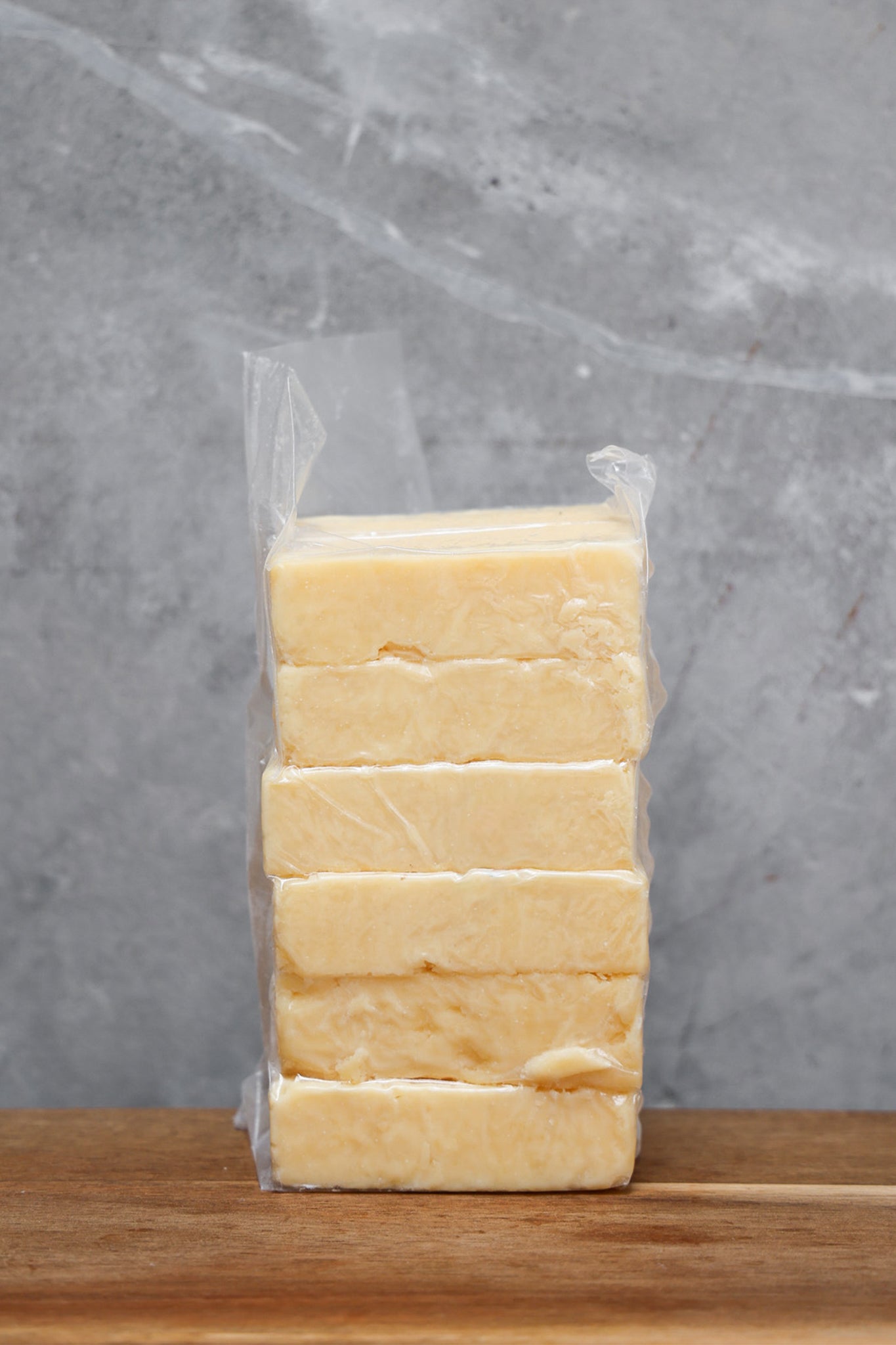 Block of Parmesan Offcuts from Eltham Cheese Bar in a clear plastic bag on a wooden surface with a gray background